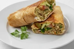 Vegan grilled falafel wrap with hummus, tahini, vegetables, caramelised onion, and pomegranate molasses.